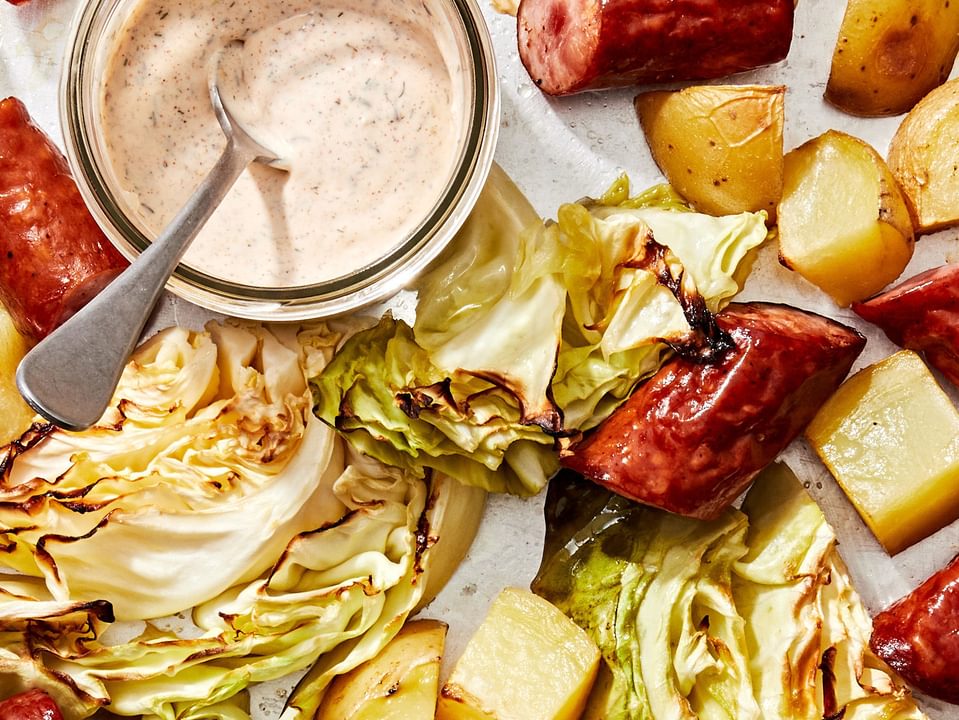 roasted cabbage, sausage and potatoes on a rimmed baking sheet wit a jar of homemade sour cream sauce for serving