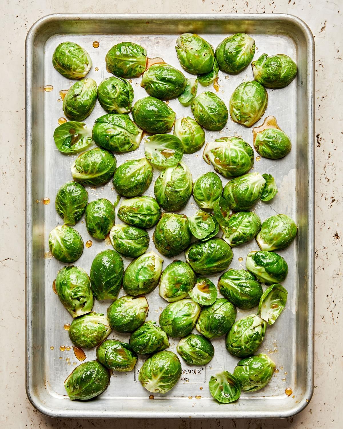 Brussels sprouts tossed with olive oil, brown sugar, maple syrup, lemon juice, salt, and cayenne on a baking sheet
