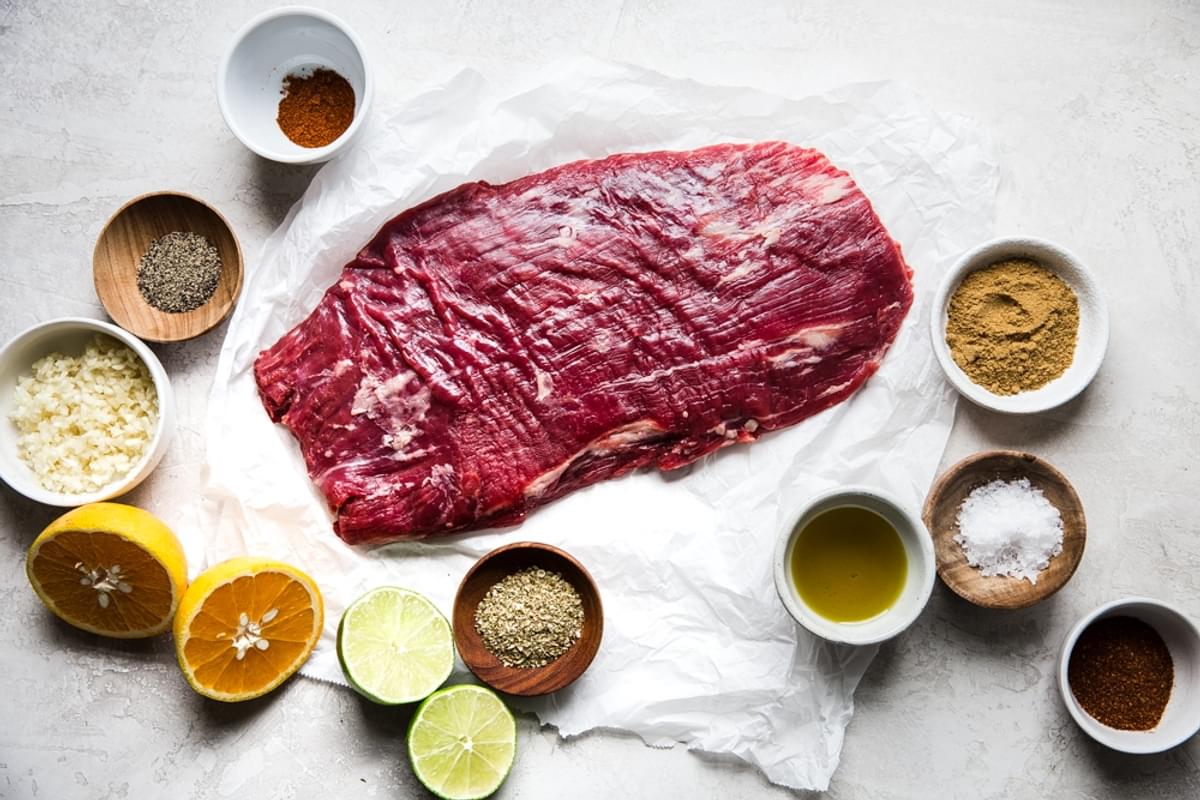 flank steak on parchment paper, orange, lime, olive oil, salt, cumin, chili powder, garlic