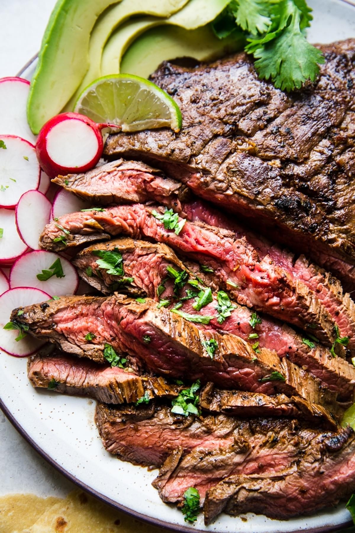 grilled skirt steak for Carne asada on a plate with avocado, lime, radish, cilantro and tortillas