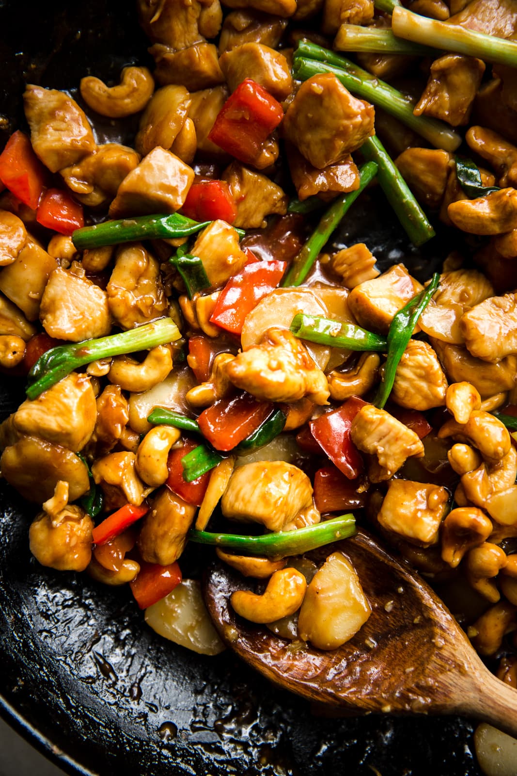 cashew chicken recipe with cashew chicken sauce in a pan being stirred with a wooden spoon.