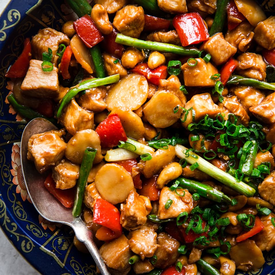 homemade cashew chicken recipe with bell pepper, garlic, ginger, green onions and soy sauce in a bowl with a spoon