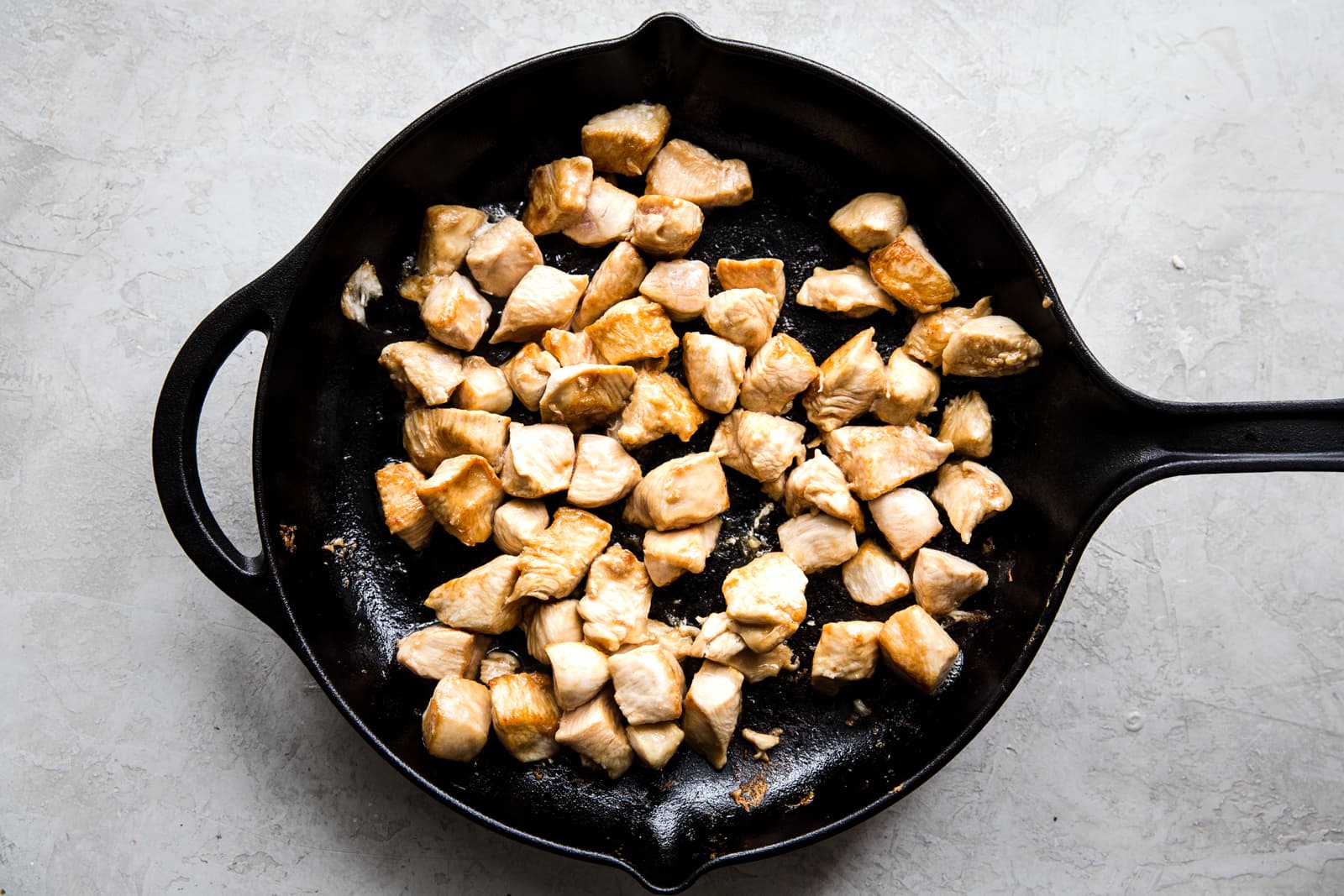 chicken marinated in cornstarch, salt and soy sauce, being cooked in a large black skillet