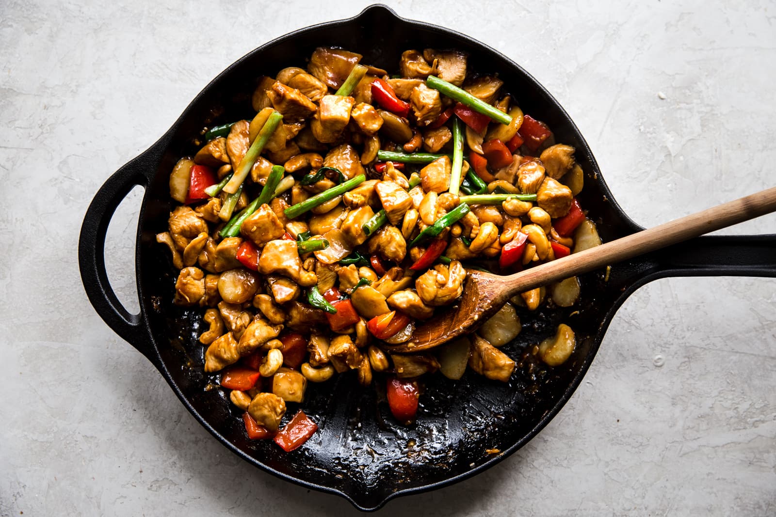 homemade cashew chicken recipe in a skillet with red bell peppers, green onions and water chestnuts.
