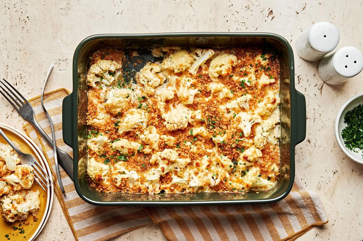 cauliflower au gratin made with Parmesan & Gruyèred topped with toasted breadcrumbs being scooped out of a baking dish