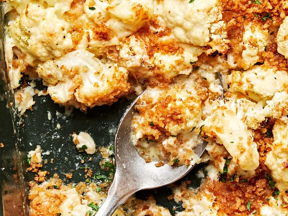 cauliflower au gratin made with Parmesan & Gruyèred topped with toasted breadcrumbs being scooped out of a baking dish