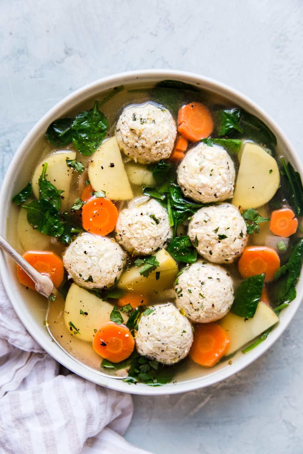 chicken meatball soup with spinach, carrots, potatoes in a bowl with a spoon