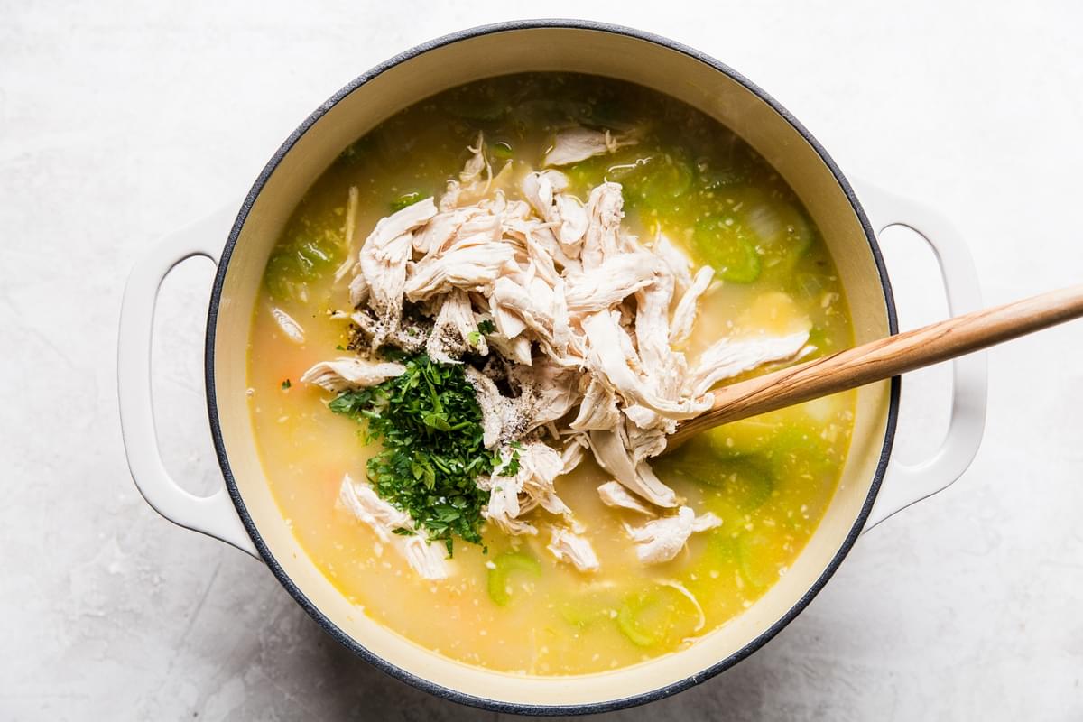 shredded chicken, chicken stock, carrots, onion and celery in a soup pot with a wooden spoon