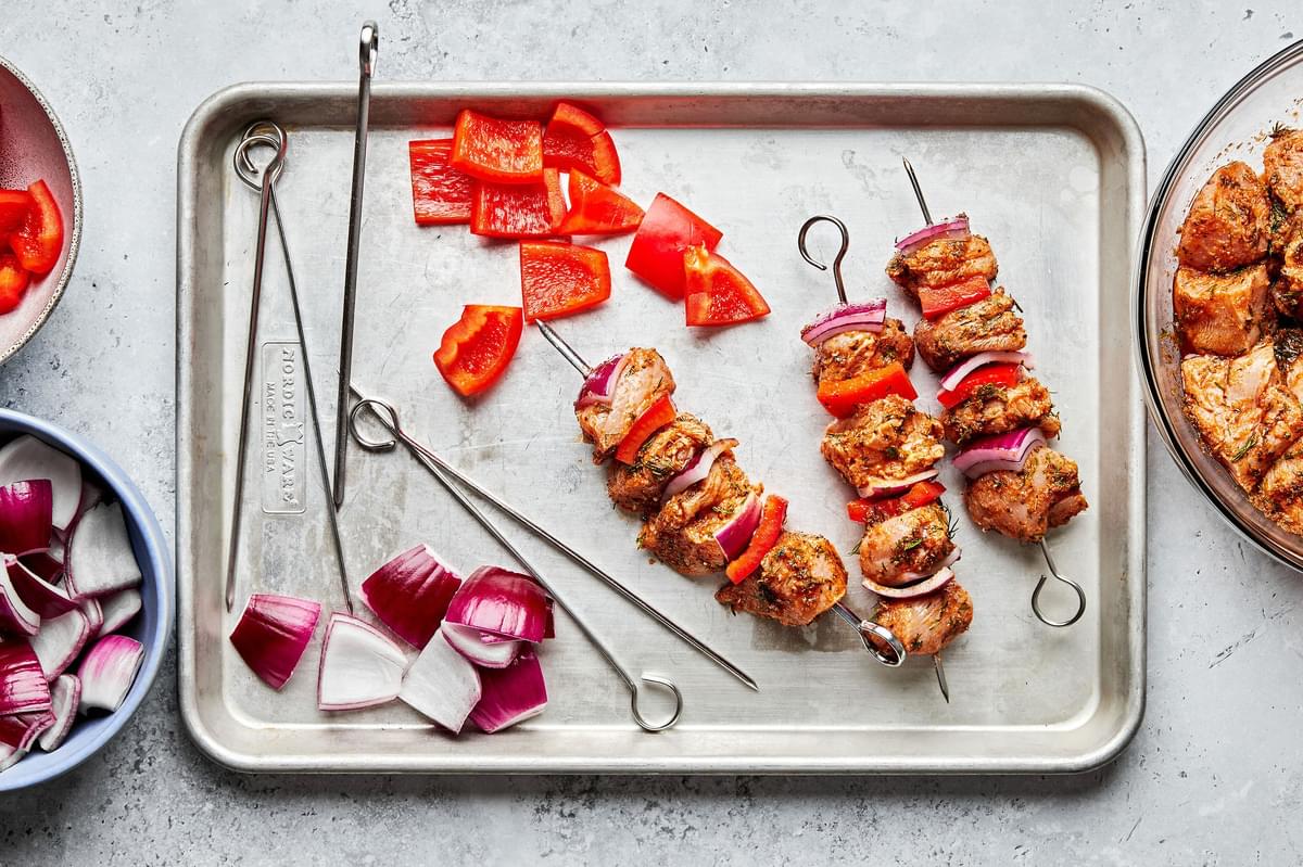 marinated chicken, bell pepper and red onion being threaded on metal skewers