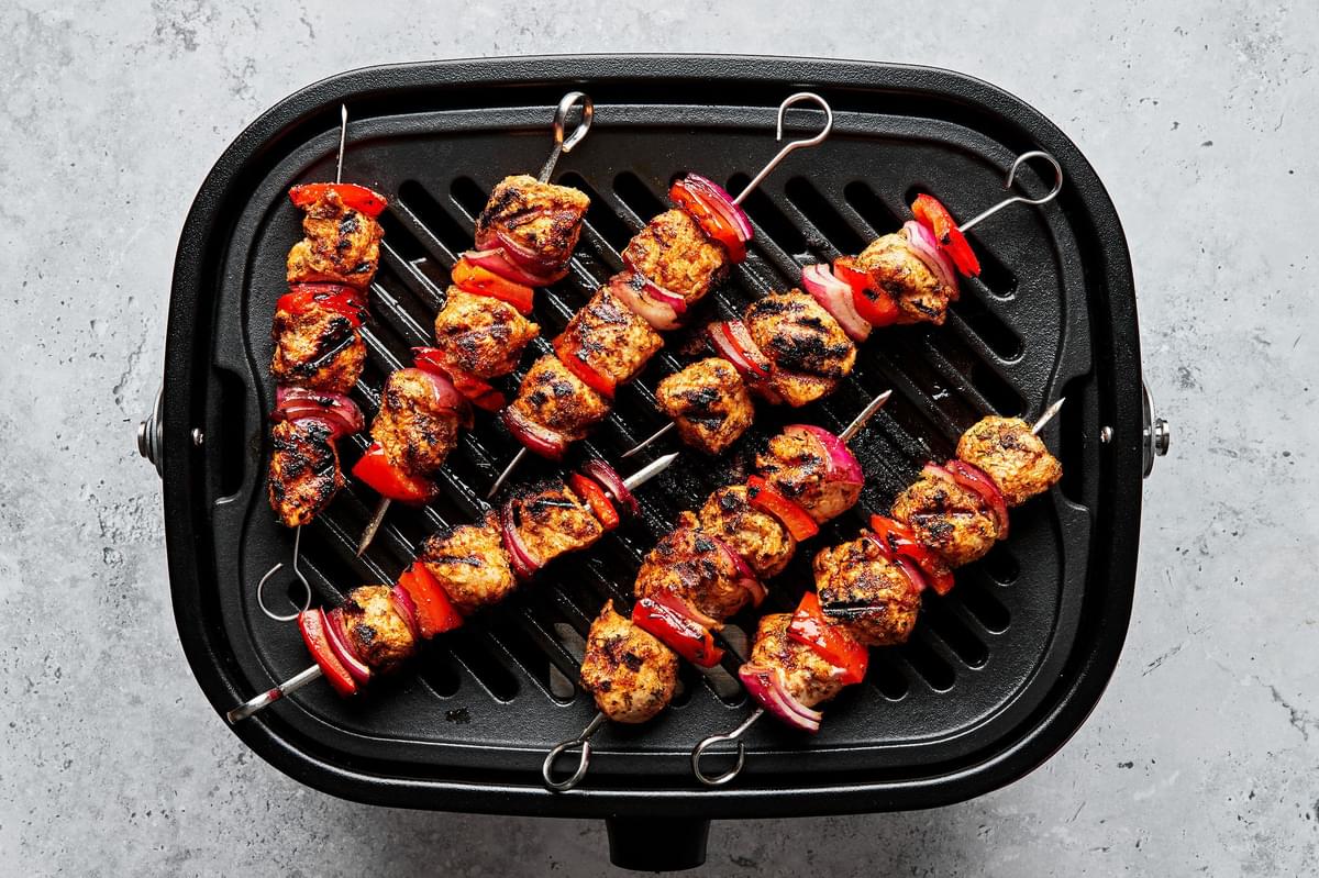 chicken kebabs with bell pepper and red onion being cooked on a grill