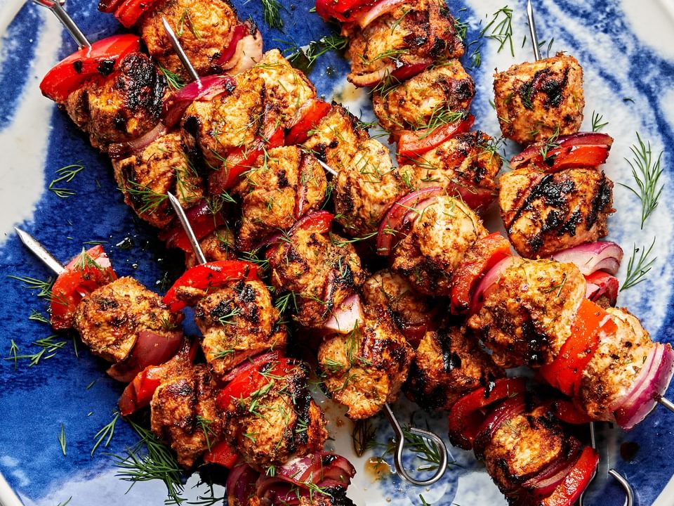 chicken kebabs with bell pepper and red onion on a serving plate served with bowls of dill sauce and romesco sauce