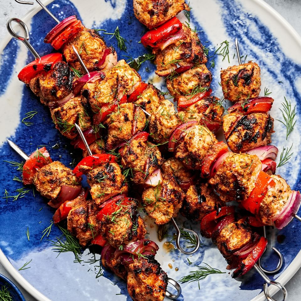 chicken kebabs with bell pepper and red onion on a serving plate served with bowls of dill sauce and romesco sauce