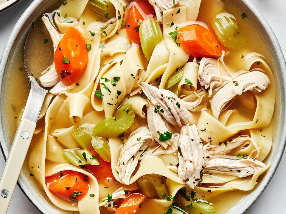 a bowl of homemade chicken noodle soup topped with parsley and pepper served with crusty bread
