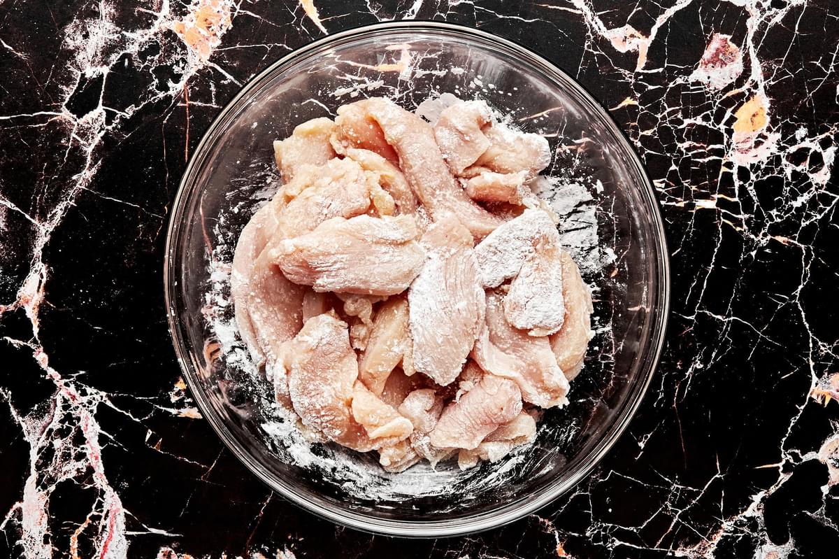 sliced chicken being tossed with salt and corn starch
