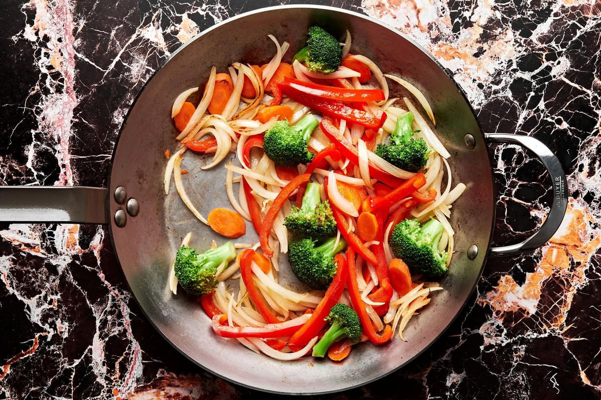 broccoli, onion, bell pepper, and carrots being cooked in oil in a skillet