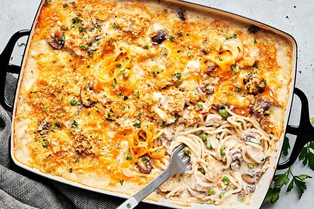 chicken tetrazzini being scooped out of a baking dish made with, mushrooms, peas, cream sauce, cheddar, Parm and panko