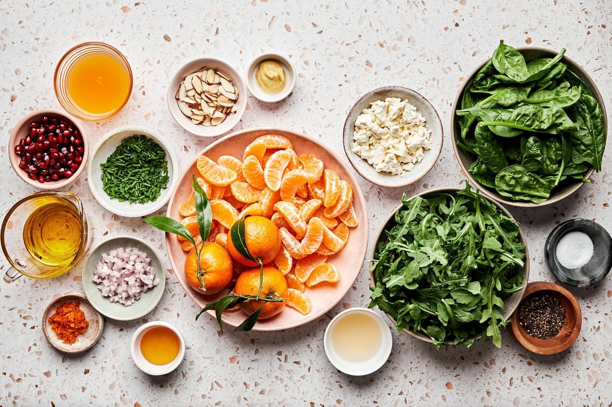 ingredients for a christmas salad in prep bowls: spinach, arugula, feta, clementines, pomegranates, almonds and chives