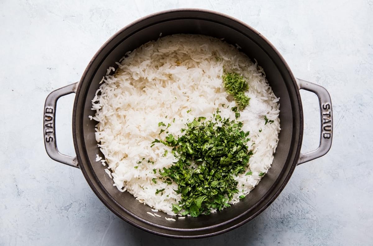 white rice being tossed with cilantro, lime zest and lime juice in a pot
