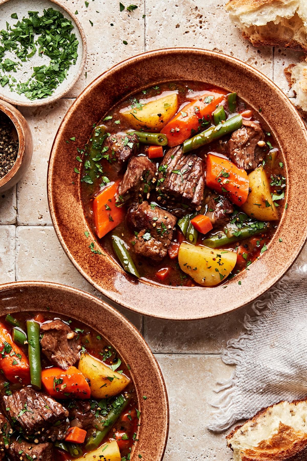 classic beef stew with green beans, potatoes and carrots sprinkled with parsley in a bowl served with rustic bread