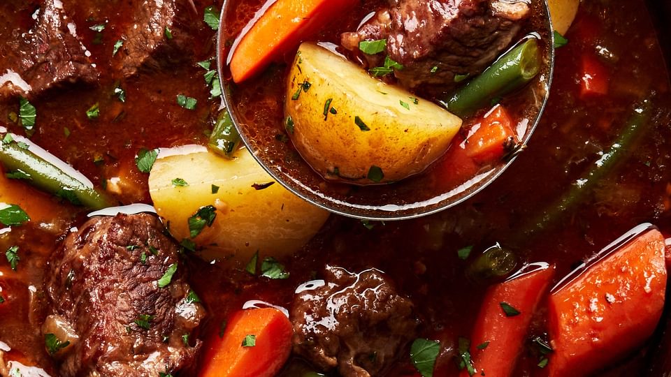 classic beef stew with potatoes, carrots and green beans being scooped out of a pot with a ladle