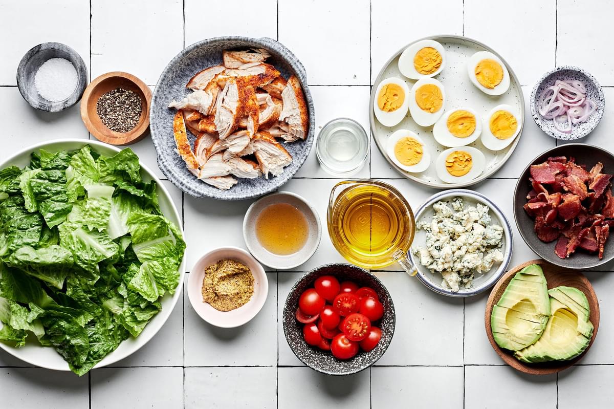 romaine, chicken, hard boiled eggs, bacon, avocado tomatoes, blue cheese and shallot vinaigrette ingredients in prep bowls