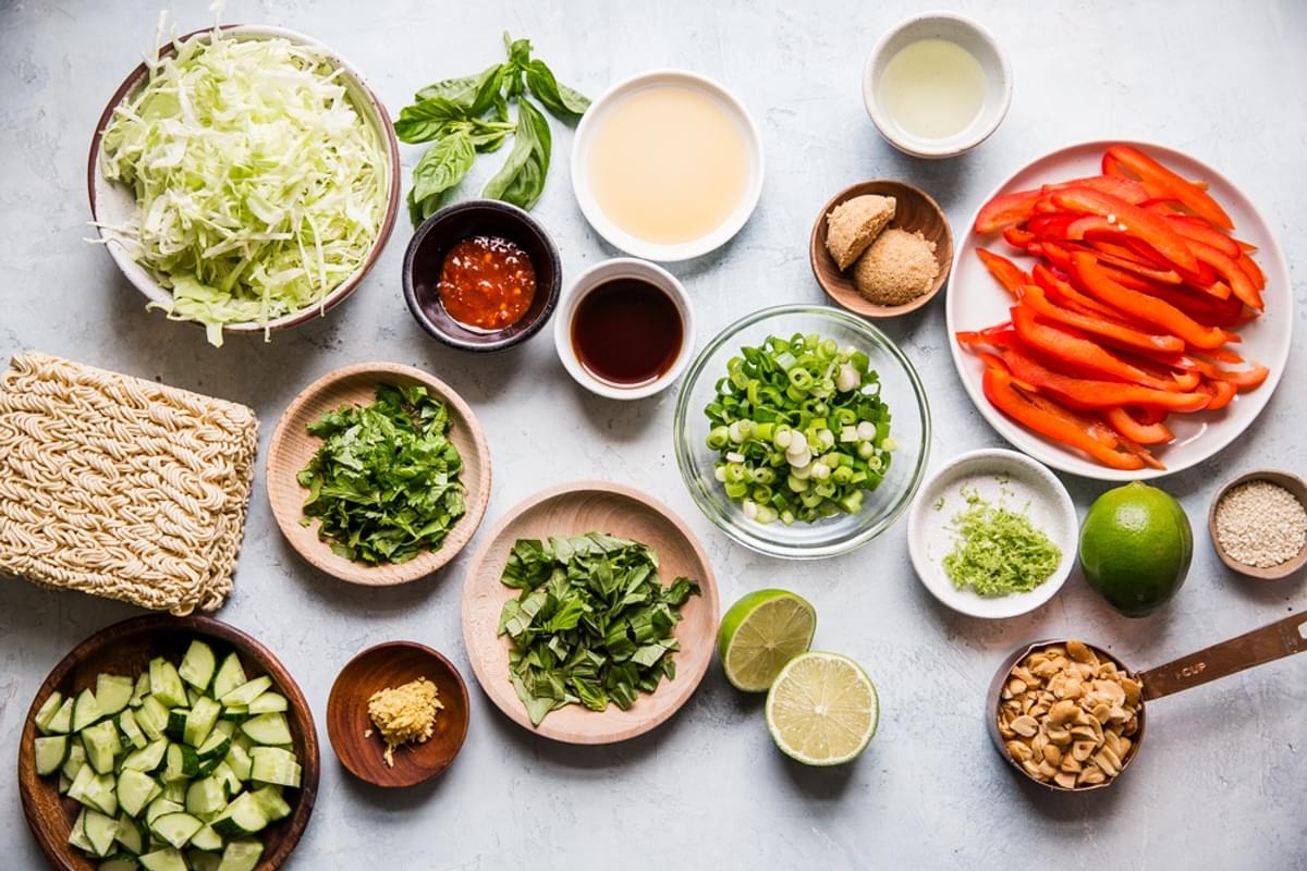 ingredients laid out for ramen salad ginger, lime, peanuts, bell peppers, cabbage, cilantro, basil, fish sauce, chili sauce