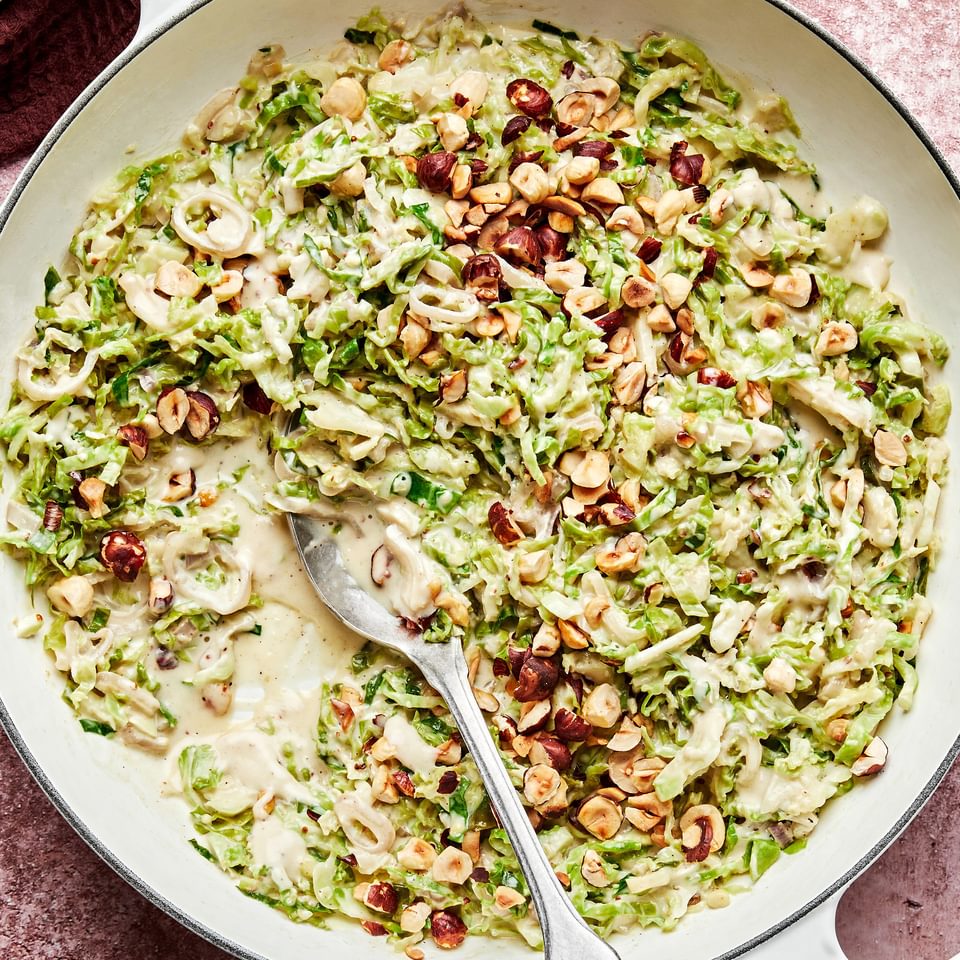 creamed brussels sprouts made with heavy cream and parmesan topped with toasted hazelnuts in a skillet