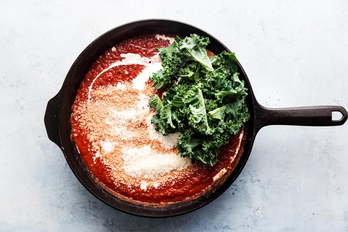 garlic, tomato paste and tomato sauce in a cast iron skillet with cream and kale
