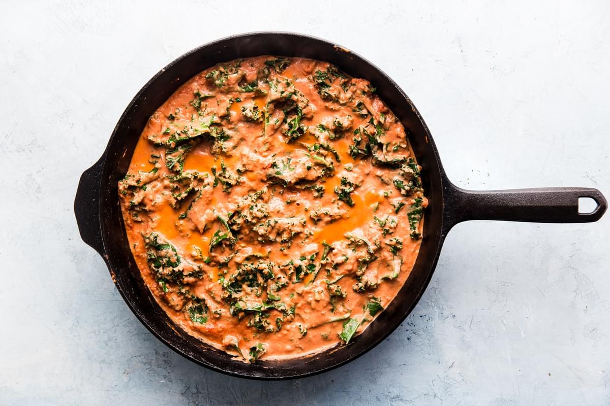 Kale and garlic simmering in a creamy tomato sauce in a large cast iron skillet
