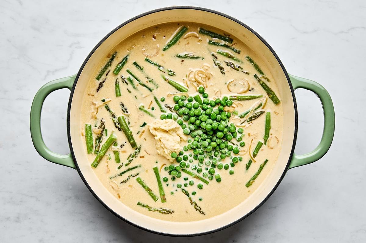 asparagus and peas being added to a skillet with cream sauce made with shallot, garlic, bouillon and Parmesan