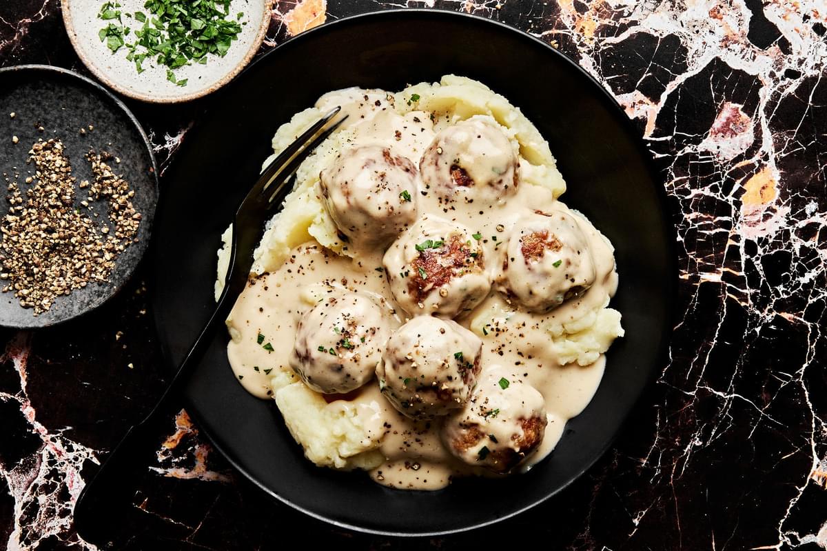a bowl of homemade turkey meatballs in cream sauce served on top of mashed potatoes and sprinkled with fresh parsley