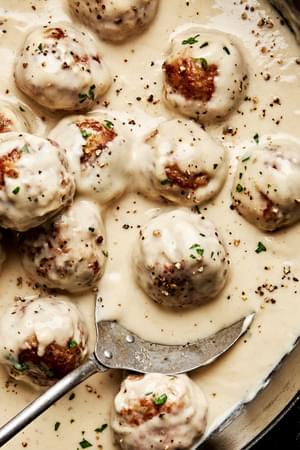 creamy turkey meatballs being scooped out of a skillet. made with breadcrumbs, spices, Worcestershire, butter and cream