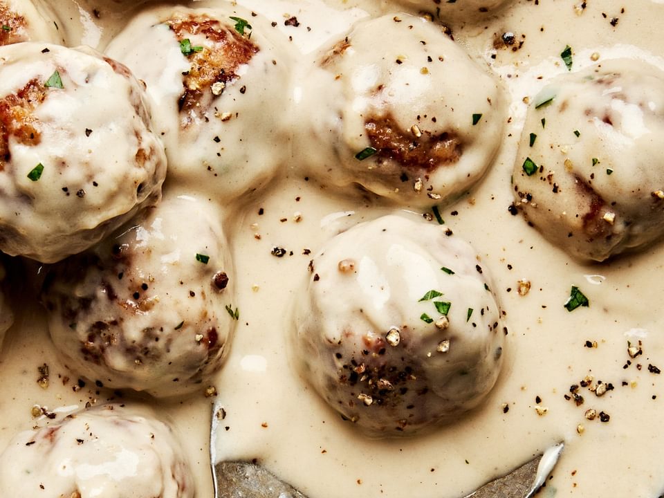 creamy turkey meatballs being scooped out of a skillet. made with breadcrumbs, spices, Worcestershire, butter and cream
