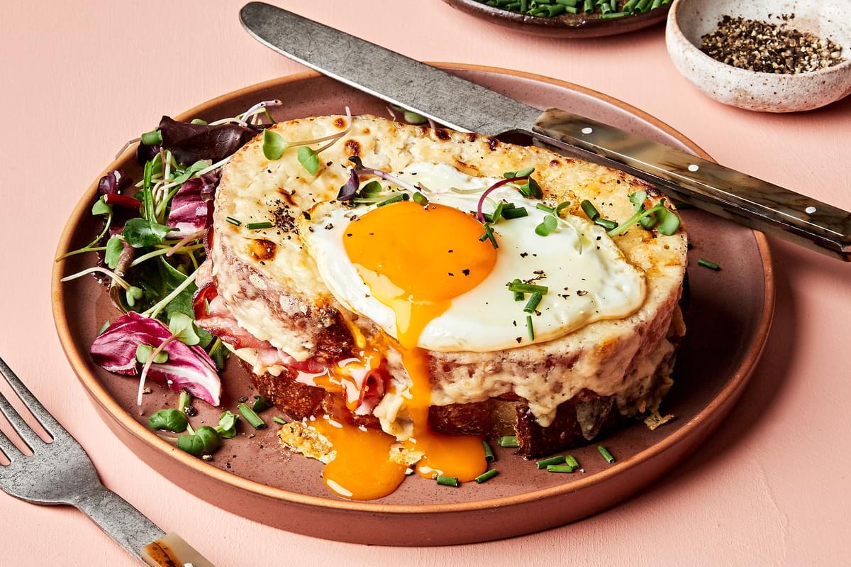 a homemade croque madame sandwich made with Béchamel sauce, ham, Gruyère & a fried egg topped with pepper, and chives