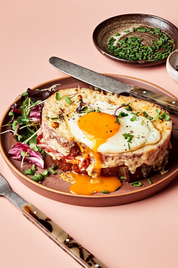 a homemade croque madame sandwich with Béchamel sauce, ham, Gruyère & a fried egg topped with pepper, and chives