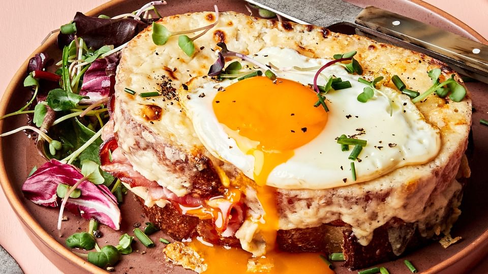 a homemade croque madame sandwich with Béchamel sauce, ham, Gruyère & a fried egg topped with pepper, and chives