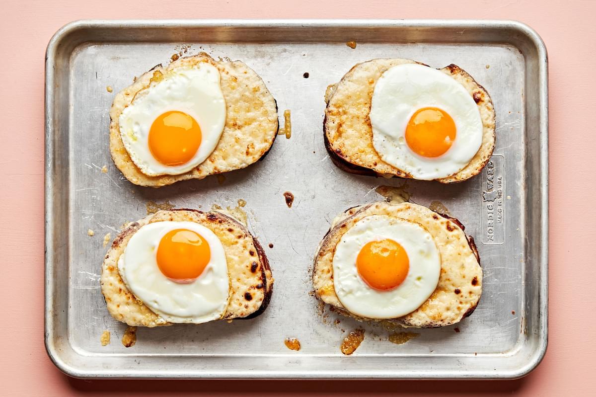 croque madame sandwiches on a baking sheet made with ham, Gruyère, homemade Béchamel sauce and topped with fried eggs