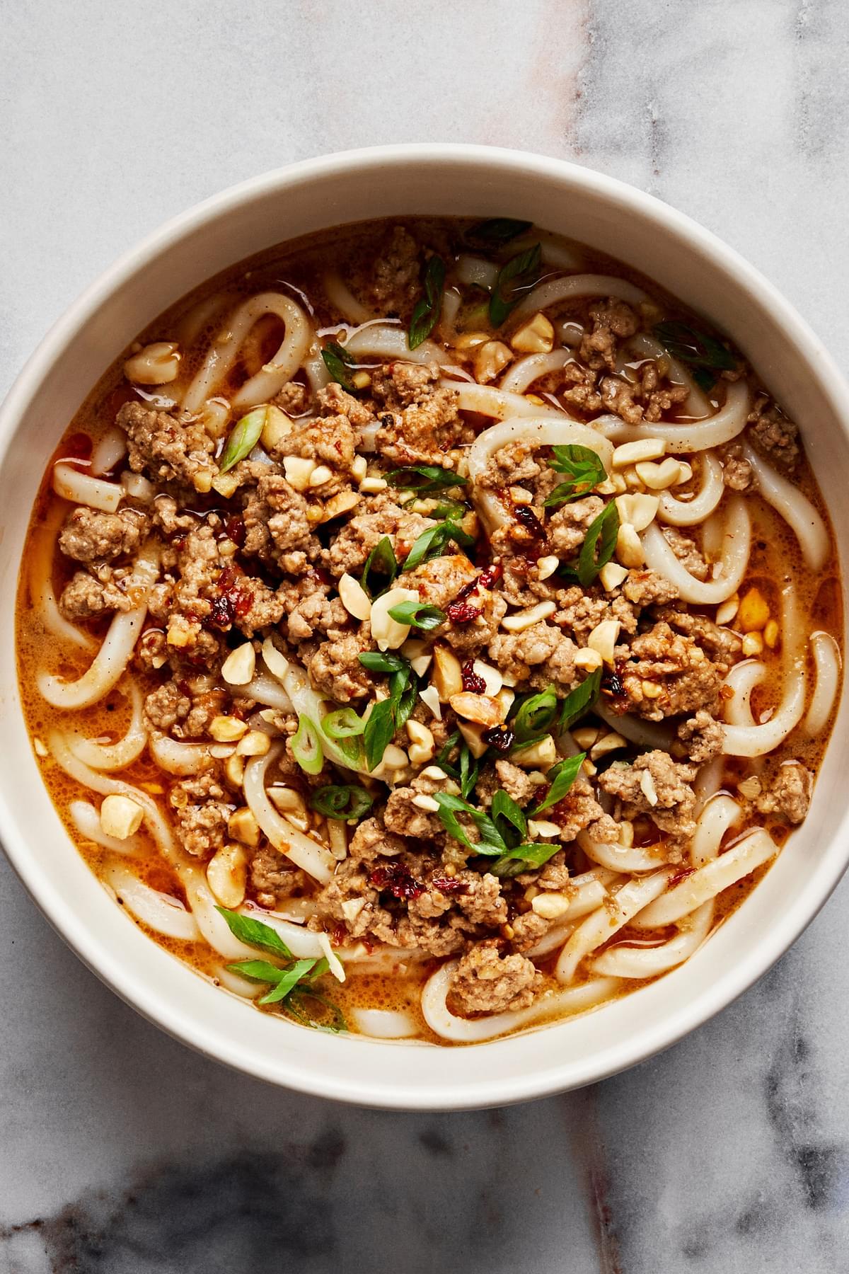 a bowl of homemade dan dan noodles sprinkled with green onions and crushed peanuts