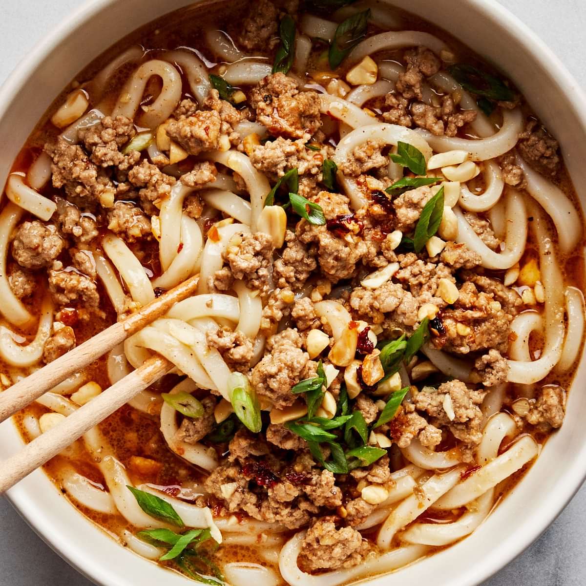 A bowl of homemade dan dan noodles sprinkled with green onions and crushed peanuts with chop sticks