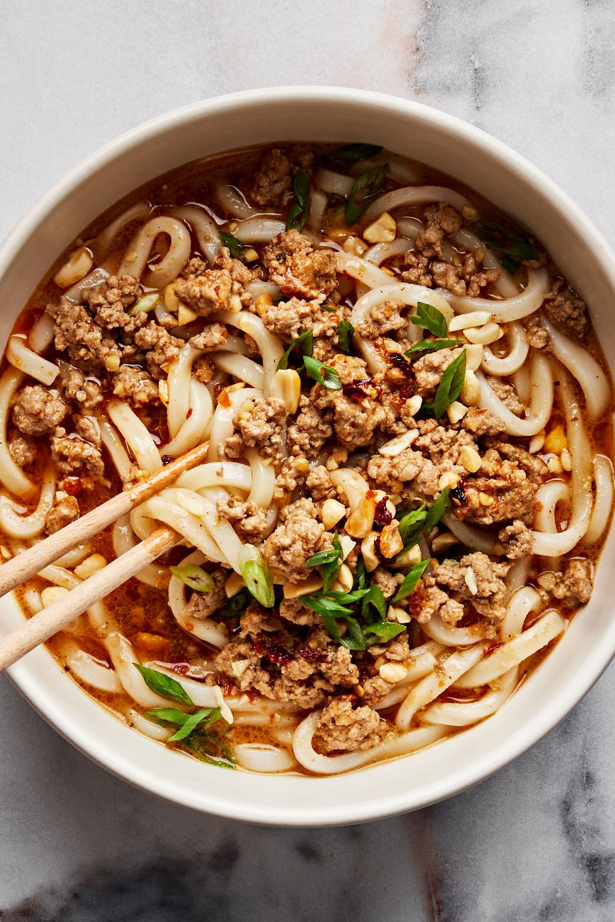 A bowl of homemade dan dan noodles sprinkled with green onions and crushed peanuts with chop sticks