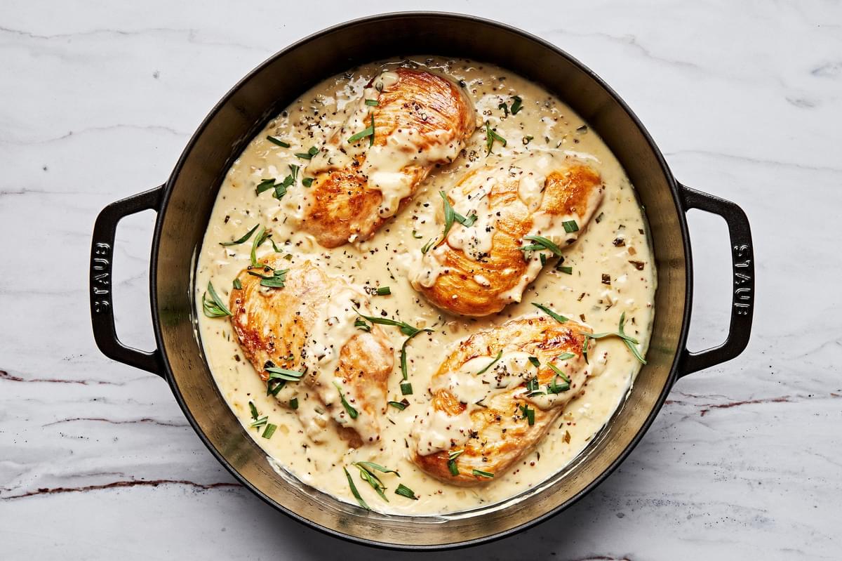 Dijon chicken in a skillet made with cream, wine, dijon and sprinkled with pepper and fresh tarragon