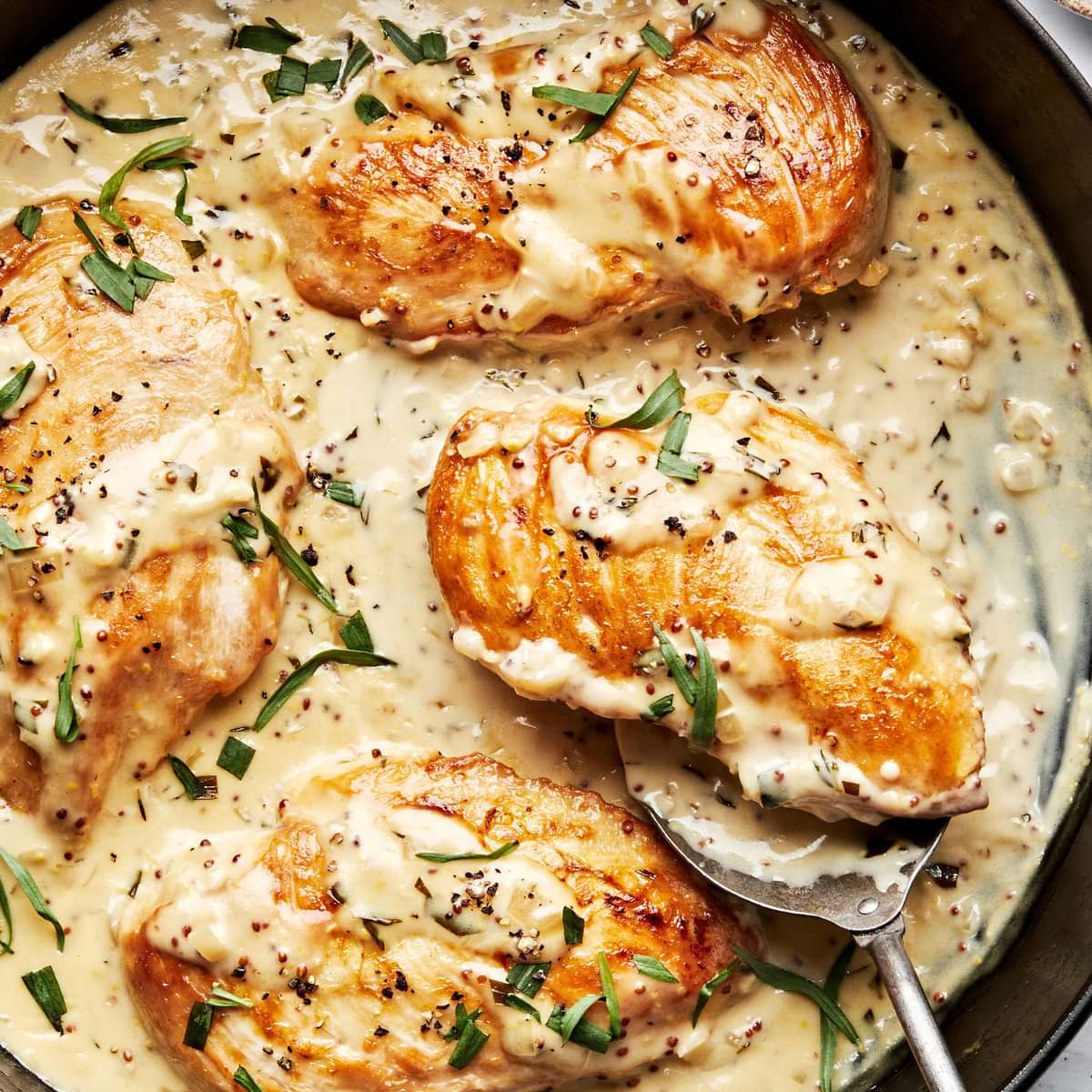 dijon chicken in a skillet made with cream, wine, dijon and sprinkled with pepper and fresh tarragon