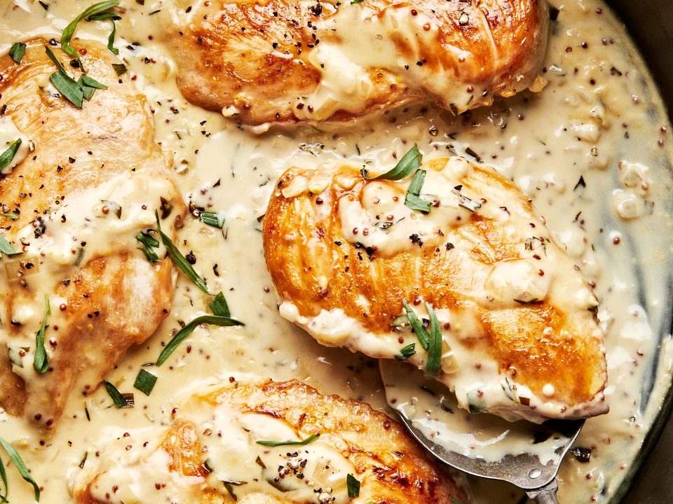 dijon chicken in a skillet made with cream, wine, dijon and sprinkled with pepper and fresh tarragon