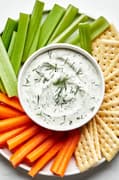 homemade dill dip in a bowl on a serving platter surrounded by celery, carrots and crackers for dipping