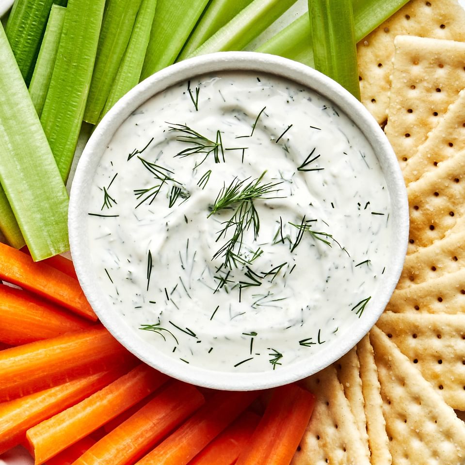 homemade dill dip in a bowl on a serving platter surrounded by celery, carrots and crackers for dipping