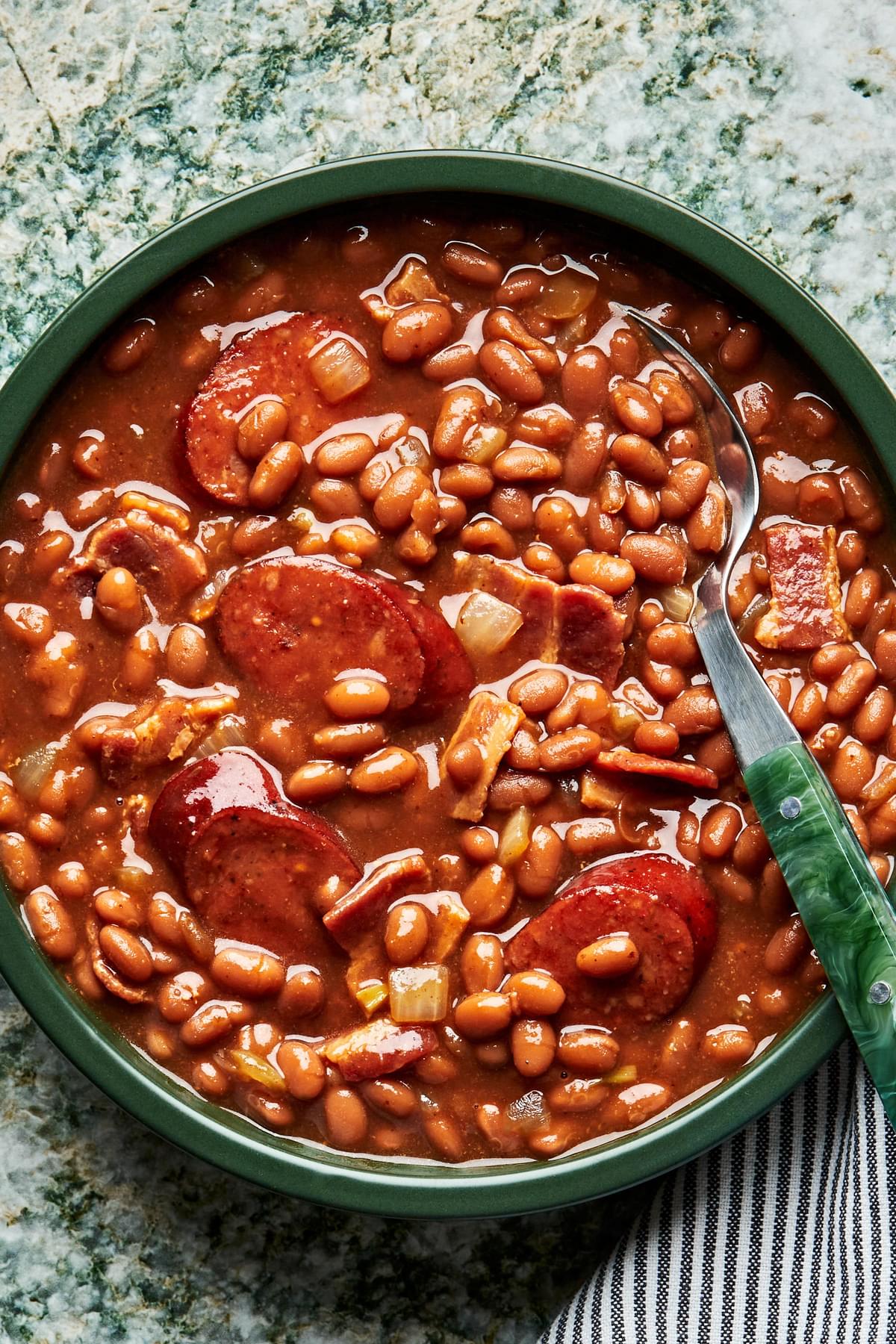 dressed up baked beans in a serving bowl. made with bacon, sausage, onion, brown mustard, molasses, maple, ketchup & vinegar