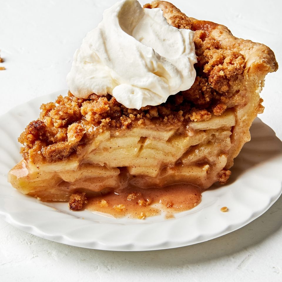 a slice of homemade Dutch apple pie topped with a dollop of whipped cream on a plate