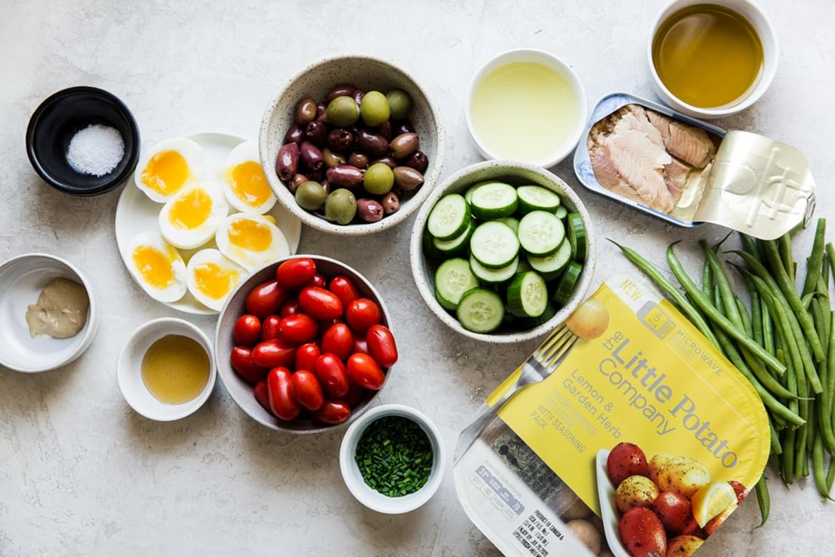 Ingredients laid out for easy nicoise salad potatoes, tuna fish, tomatoes, olives and soft boiled eggs.