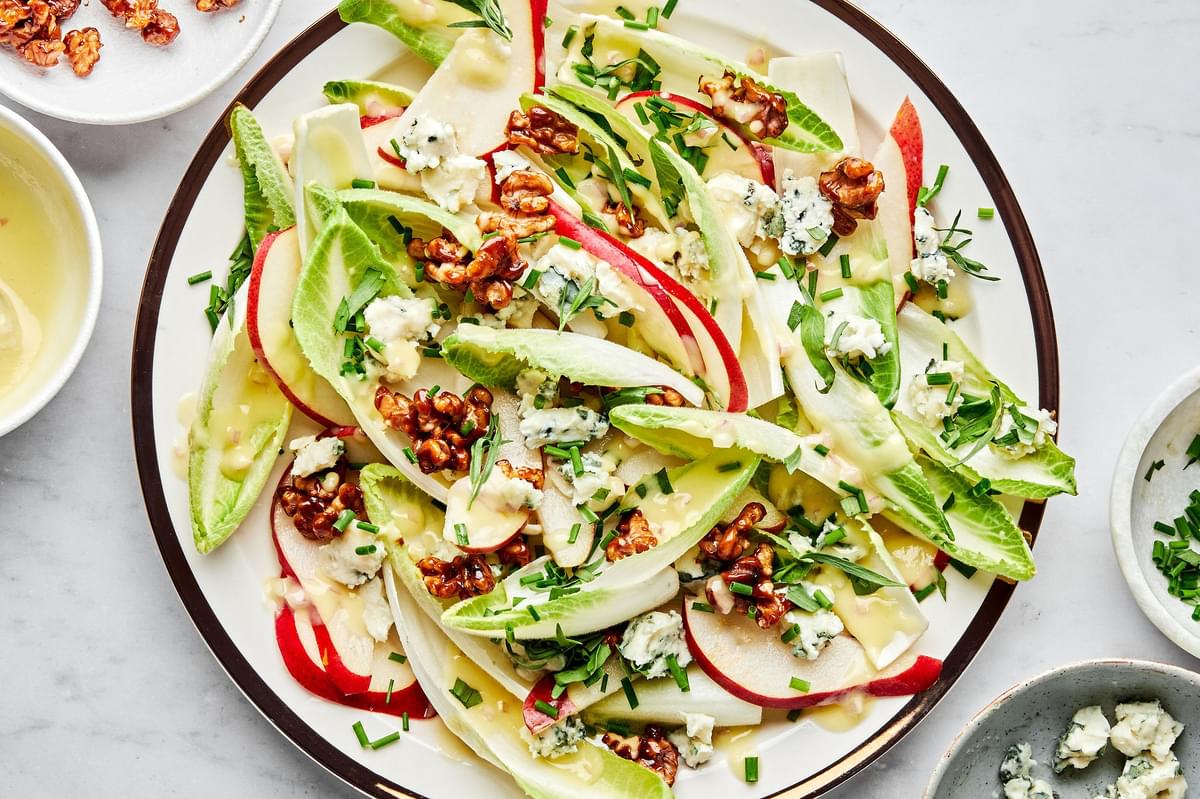 An Endive and Roquefort Salad sprinkled with candied walnuts and fresh chives on a serving plate