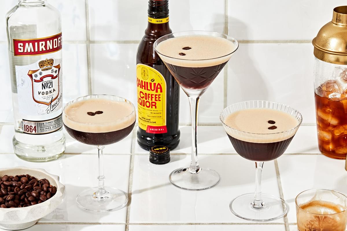 3 espresso martinis on the counter surrounded by bottles of vodka and kahlua and a bowl of coffee beans for garnishing
